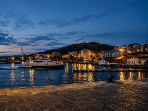 Tramonto sul porto di Reggio Calabria con lungomare illuminato, traghetto e paesaggio urbano collinare