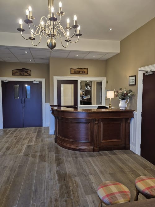 Elegant hotel reception area at Sliabh Beagh Hotel with dark wood curved desk, chandelier, and wood-plank flooring.