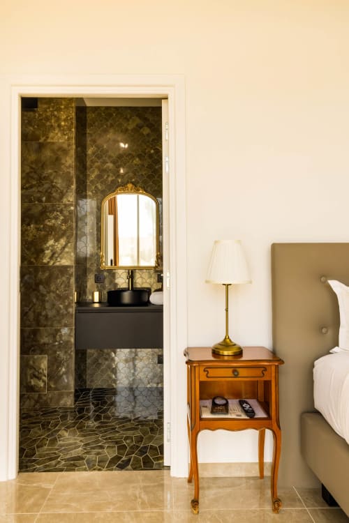 Salle de bains attenante élégante aux carreaux dorés et vanité noire, adjacente à la chambre avec lampe de chevet à l'Hôtel Villa Martini