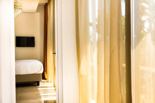 Chambre d'hôtel moderne à la Villa Martini Ajaccio avec vue mer, lit, rideaux dorés et TV écran plat