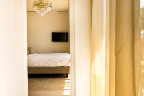Élégante chambre à l'Hôtel Villa Martini à Ajaccio avec literie blanche, lustre, TV murale et rideaux crème