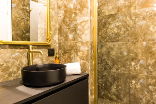 Salle de bain luxueuse de l'Hôtel Villa Martini à Ajaccio avec vasque noire, robinetterie dorée et carrelage effet marbre
