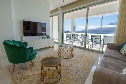 Modern living room in Horta, Açores with green velvet chair, sea view balcony overlooking mountain, flat-screen TV, and gold