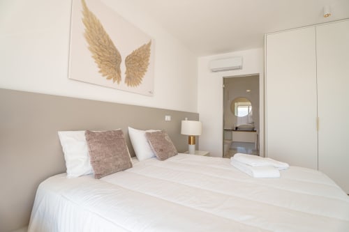 Modern bedroom in Suites Avenue Lux Apartments, Horta, with white bed, beige headboard, gold wing artwork, and ensuite