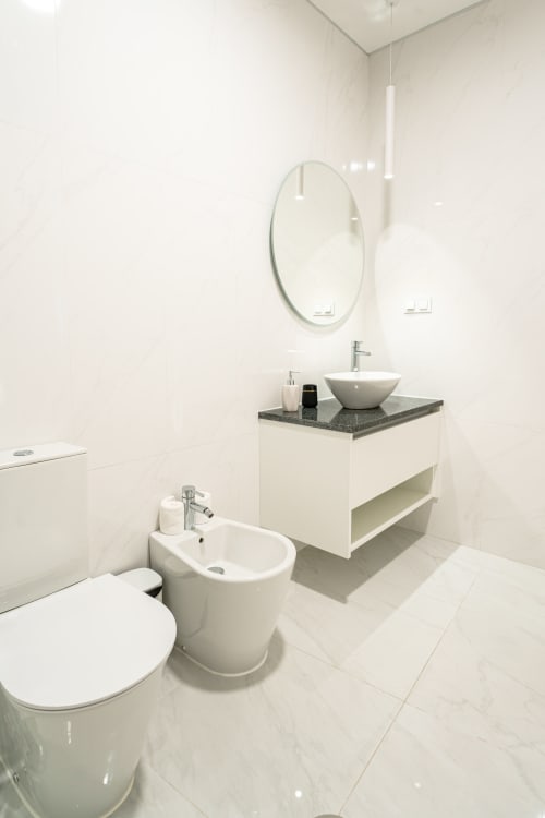 Modern bathroom at Suites Avenue Lux Apartments in Horta with white fixtures, round mirror, and dark countertop