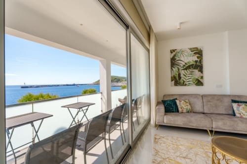 Luxury apartment living room with sea view balcony overlooking Horta harbor, modern furnishings and tropical decor