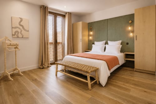 Chambre moderne à la Villa Alora à Calenzana avec parquet, mur d'accent vert et vue sur les montagnes depuis le balcon
