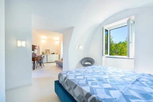 Camera moderna presso Origenes Rooms B&B in Italia con biancheria blu decorata, pareti curve e finestra con vista sul verde