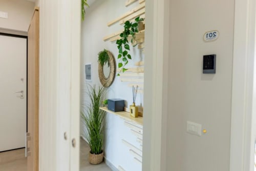 Corridoio moderno dell'Aurum Nolana Suites Pompeii BnB con pareti bianche, scaffali in legno, piante decorative e arredamento minimalista