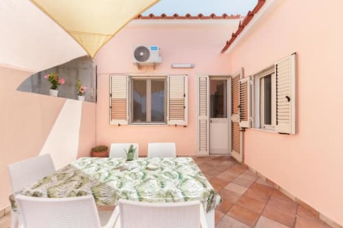 Terrazza rosa con tavolo da pranzo, piante in vaso e finestre con persiane presso Origenes Rooms B&B in Italia
