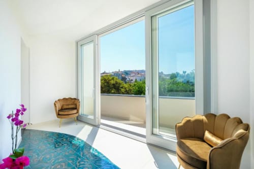 Luminosa camera moderna presso Origenes Rooms con poltroncine dorate, tappeto turchese e balcone con vista sulla campagna italiana