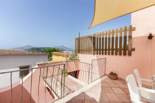Terrazza soleggiata di Origenes Rooms con vista montagna, sdraio, ombreggiatura in legno e architettura dai toni rosa in Italia