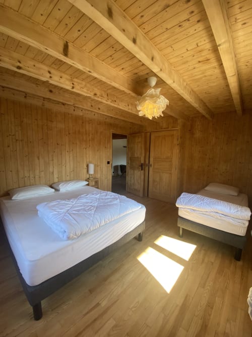 Spacious wooden bedroom in French Alps chalet with queen bed, single beds, exposed beams, and mountain views
