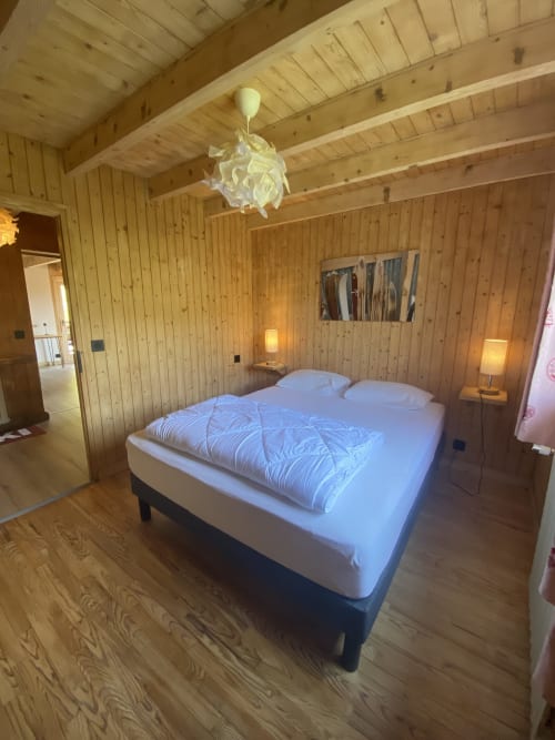 Cozy wood-paneled bedroom with queen bed, white bedding, and pendant lamp in alpine chalet apartment in