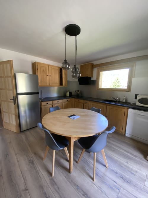 Modern kitchen and dining area with round wooden table, black chairs, stainless steel appliances, and pendant lighting in