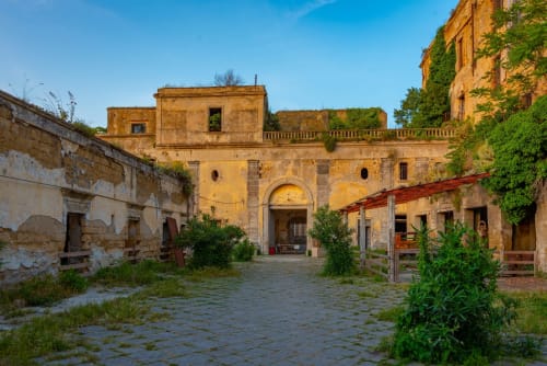 Historic stone courtyard with ivy-covered buildings at Origenes Rooms B&B in Italy, featuring arched entrance and
