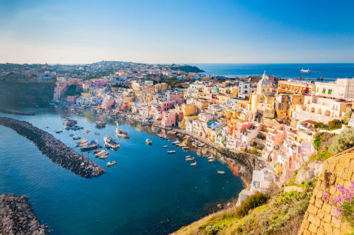 Colorful coastal town Procida with pastel buildings, boats, and Mediterranean Sea at Origenes Rooms