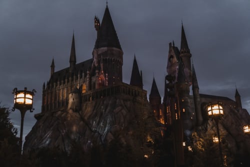 Castillo gótico iluminado con múltiples torres al atardecer, que evoca Hogwarts, ubicado cerca de Lyon, Francia