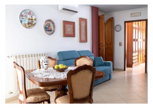 Ampio soggiorno dell'appartamento a Lipari a Milazzo con divano blu, tavolo da pranzo, piatti decorativi e vista sulla città