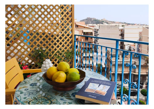 Balcone con grigliato giallo, agrumi freschi e ringhiera azzurra con vista sulla città di Milazzo - StaysinSicily