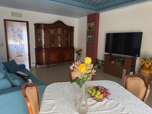 Soggiorno dell'appartamento Lipari a Milazzo con tavolo da pranzo, fiori, TV schermo piatto, mobili in legno e divano teal