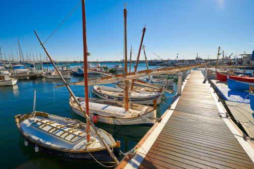 Traditional wooden fishing boats moored at Mediterranean harbor in Spain, clear blue water and wooden dock pier