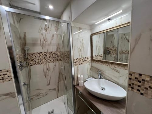 Bagno moderno dell'Hotel Ercoli House Roma con piastrelle in marmo, dettagli in mosaico, doccia in vetro e lavabo a bacinella
