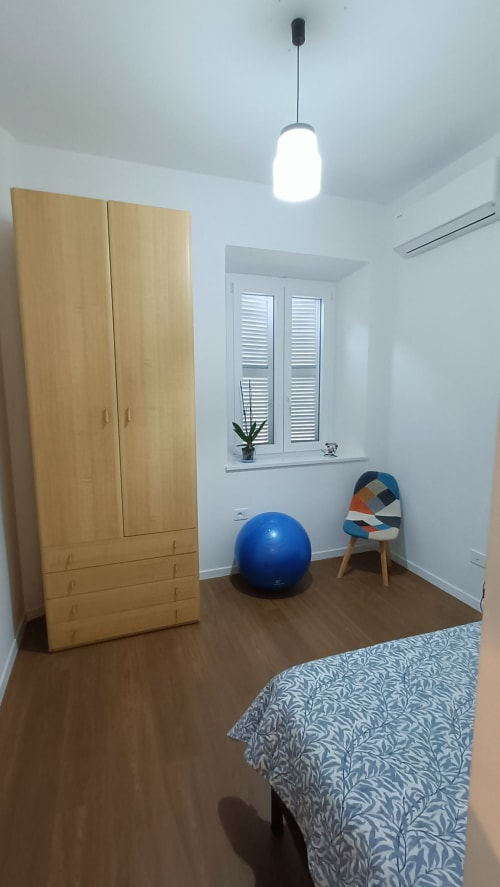 Camera moderna a Roma Casa Tua con armadio in legno, palla fitness, sedia colorata e illuminazione a sospensione