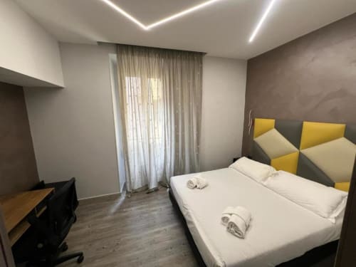 Moderna camera matrimoniale all'Hotel Ercoli House Roma con testata giallo e grigio, biancheria bianca e design geometrico a parete