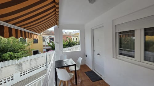 Terraza cubierta con toldo rayado, mesa de comedor y sillas blancas con vistas al jardín de Monica Socarici, Benicàssim