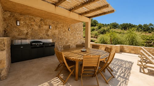 Espace de repas en plein air à Villa Alora avec table en bois, murs en pierre et cuisine de jardin à Calenzana
