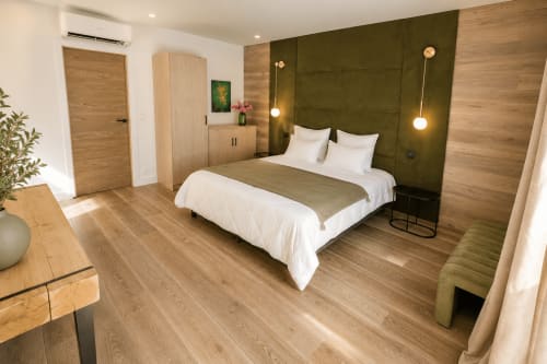 Chambre moderne à la Villa Alora à Calenzana avec tête de lit vert olive, draps blancs, parquet et luminaires suspendus
