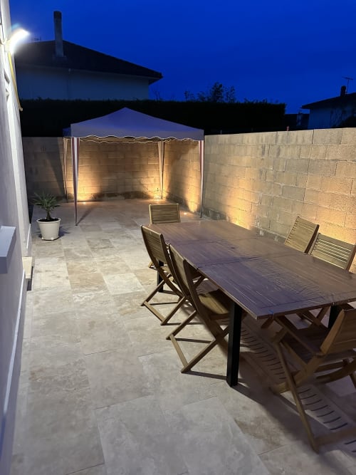 Terrasse illuminée de la Villa des Palmiers à Villeneuve-sur-Lot avec table à diner, chaises et gazebo au crépuscule
