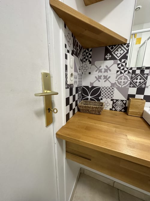 Élégant coin de salle de bain aux carrelages géométriques noir et blanc, plan de travail en bois et accessoires en laiton à la Villa des Palmiers