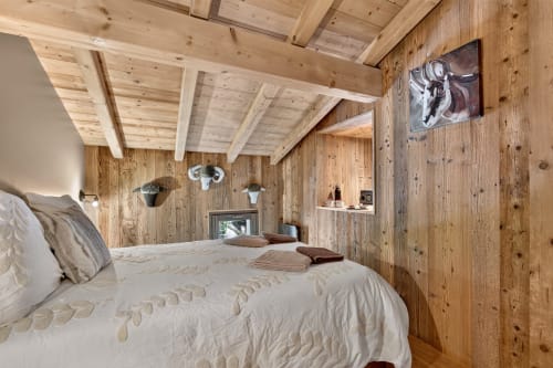 Chambre rustique avec poutres apparentes, lit queen-size, parure crème, cheminée et décoration murale à L'Alp'In en Montagne