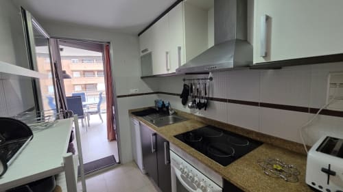 Cocina moderna en Benicàssim con estufa eléctrica, encimeras de granito y vistas al mar desde la puerta de la terraza