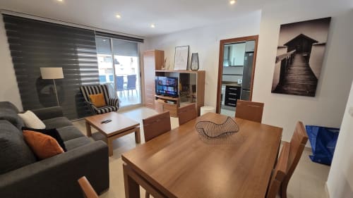Moderno apartamento frente al mar en Benicàssim con sala abierta, mesa de comedor de madera, sofá gris y vistas al mar desde el balcón