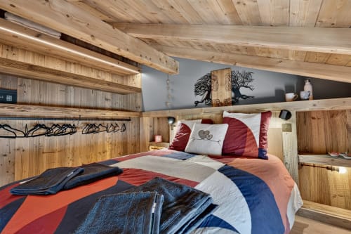 Chambre cosy en mezzanine chez L'Alp'In B&B avec literie colorée, étagères intégrées et poutres apparentes à La Plagne.