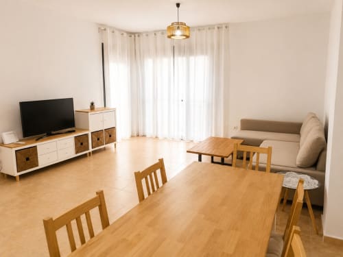 Modern living room in Alzara cottage, Sanlúcar de Barrameda, with dining table, TV, beige sofa, and bright windows