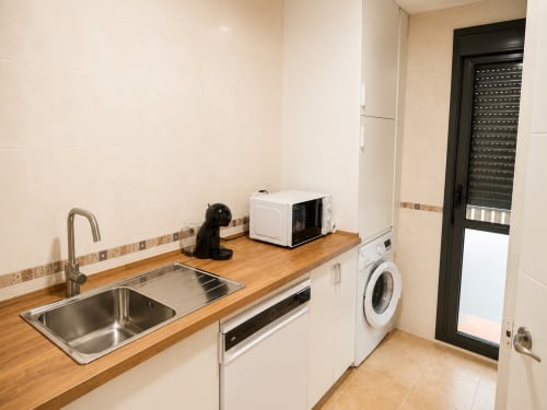 Modern kitchen with wooden countertop, sink, microwave, washing machine, and black door at Apartamentos Living Sur, Sanlúcar