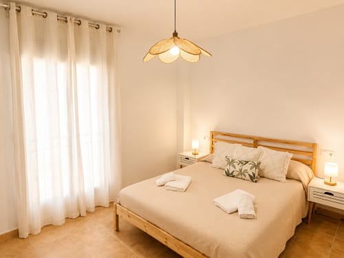 Bright bedroom at Living Sur in Sanlúcar de Barrameda with wooden bed, cream linens, pendant light, and sheer curtains