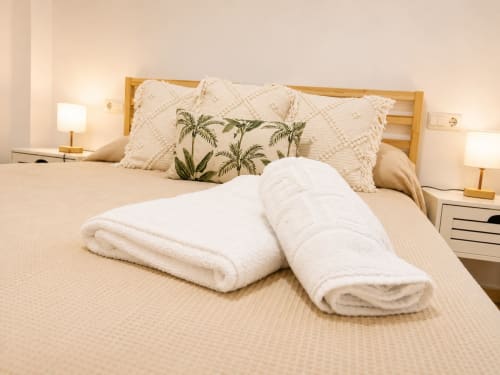 Cozy bedroom at Living Sur cottage in Sanlúcar de Barrameda with white rolled towels on bed, palm leaf pillow, and warm