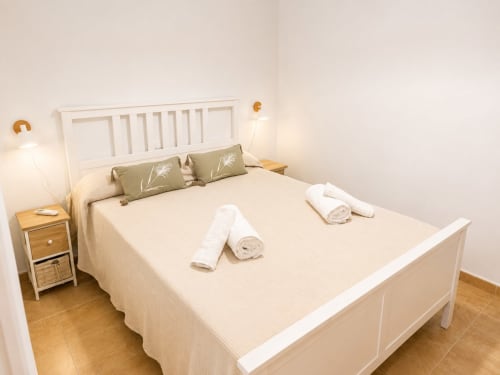 Master bedroom in Alzara cottage at Living Sur, Sanlúcar de Barrameda with white bed frame, rolled towels, and bedside lamps