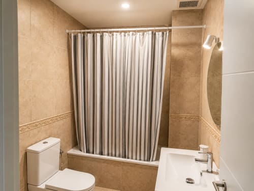 Modern bathroom with beige tile walls, white toilet, sink, mirror, and striped shower curtain in Alzara apartment at Living