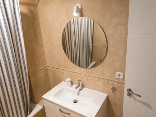 Modern bathroom in Living Sur cottage with round mirror, white sink, tiled walls, and shower curtain in Sanlúcar de Barrameda