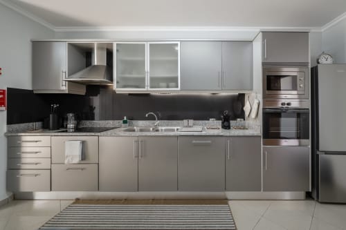Cozinha moderna com eletrodomésticos em aço inoxidável e armários cinzentos no apartamento Blue Horizon em Caniço