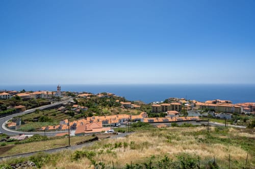 Vista costeira de Caniço com apartamentos de telhado em terracota, igreja e horizonte de mar azul na Rent-A-Key