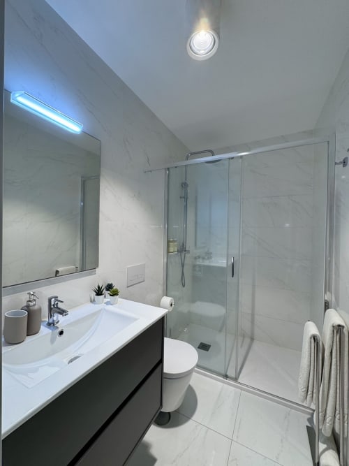 Salle de bain moderne de l'appartement RIA CENTRUM Deluxe Grey à Aveiro avec carrelage marbre, vasque, toilettes et douche vitrée