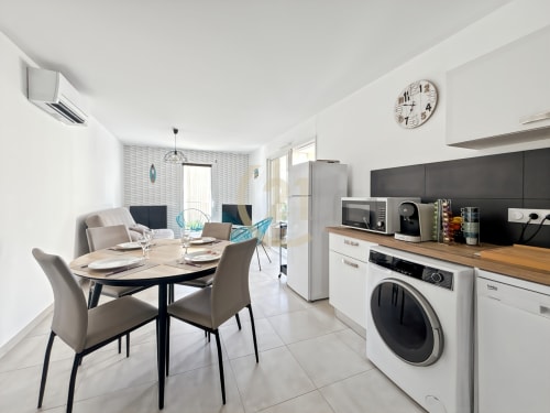 Cuisine ouverte moderne avec coin repas, lave-linge et salon dans un appartement à Calvi