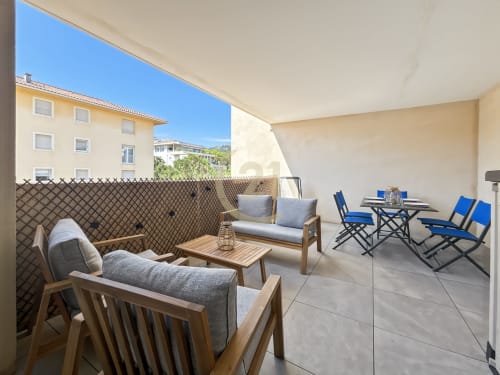 Terrasse spacieuse avec mobilier en bois, coussins bleus et vue sur la ville à Calvi, Corse